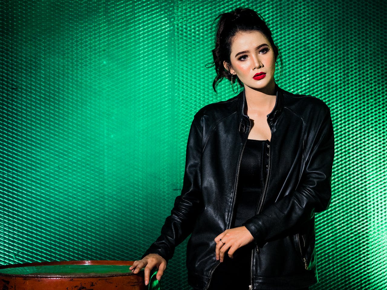 creative-02 Portrait of a fashionable woman in a black leather jacket with red lips against a green background.