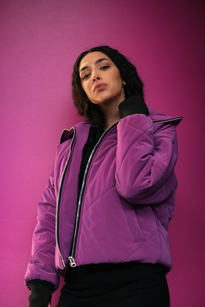 creative Stylish portrait of a woman wearing a purple bomber jacket against a vibrant pink background.