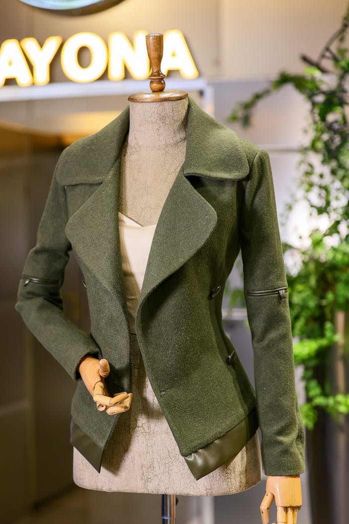 creative-03 Elegant green coat displayed on a mannequin in a modern fashion store setting.