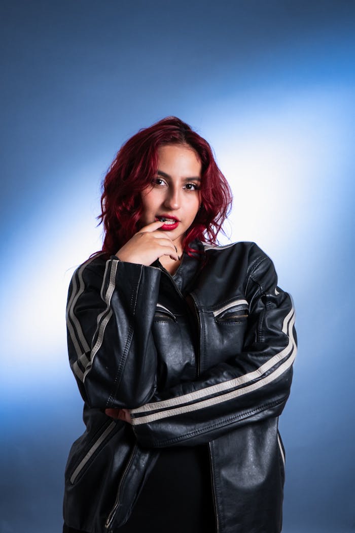 why-choose-us Striking portrait of a woman in a black leather jacket with red hair against a blue backdrop.